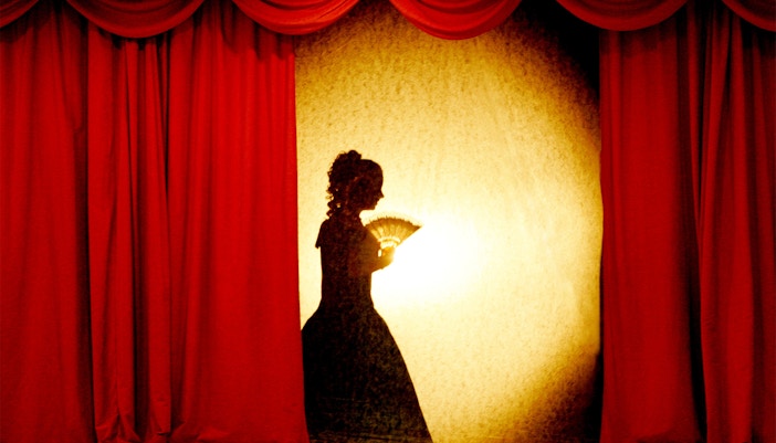 woman in theatrical costumes performing shadow theater on stage.
