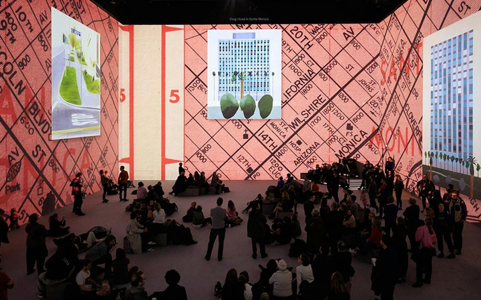 David Hockney exhibition with large digital art projections and seated audience.