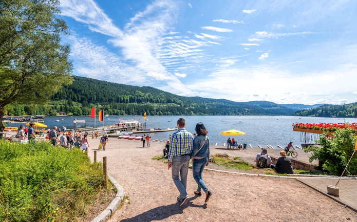 Couple walking along Lake Titisee with scenic view of Black Forest in Germany.