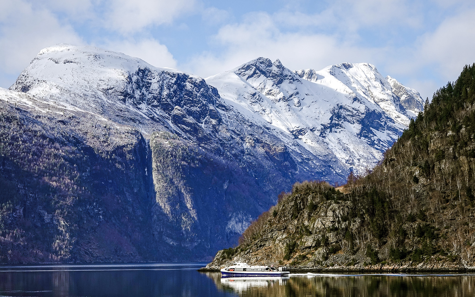 Cruise boat on Geirangerfjord with snow-capped mountains in Norway.
