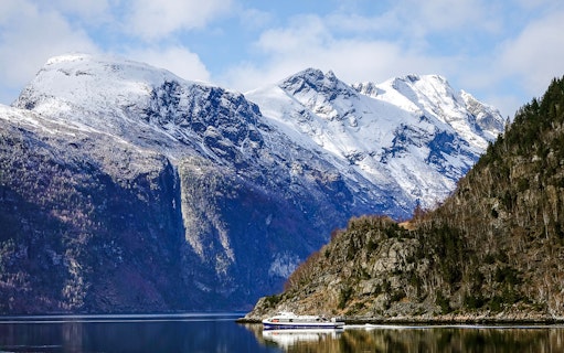 Cruise boat on Geirangerfjord with snow-capped mountains in Norway.