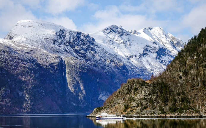 Cruise boat on Geirangerfjord with snow-capped mountains in Norway.