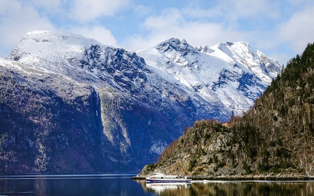 Cruise boat on Geirangerfjord with snow-capped mountains in Norway.