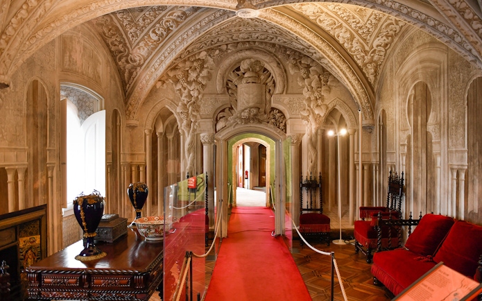 Pena Palace interior with ornate arches, red carpet, and antique furniture in Sintra, Portugal.
