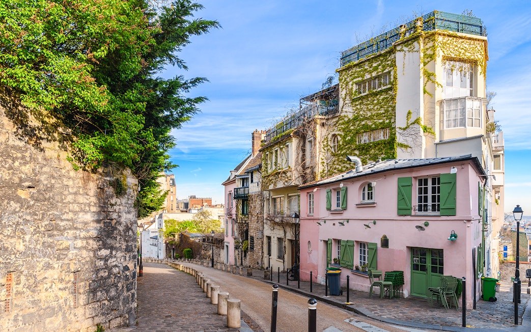 Cobblestone street in Montmartre, Paris, lined with ivy-covered buildings and a pink café.