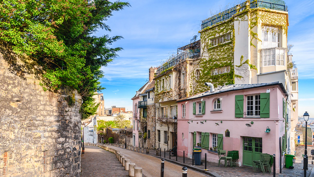 Cobblestone street in Montmartre, Paris, lined with ivy-covered buildings and a pink café.
