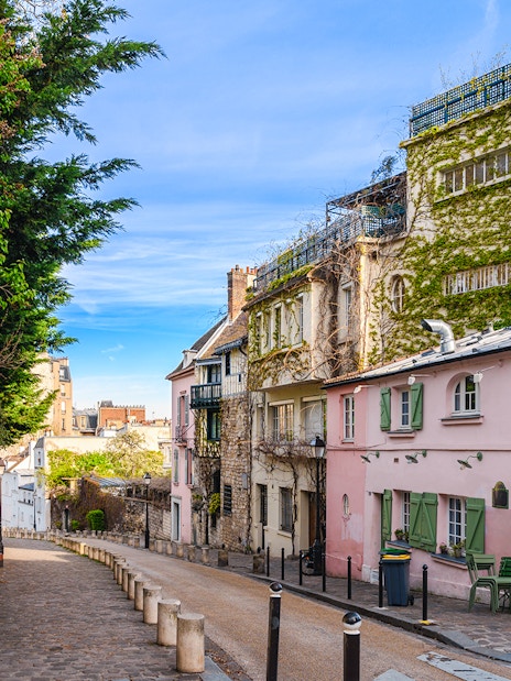Cobblestone street in Montmartre, Paris, lined with ivy-covered buildings and a pink café.