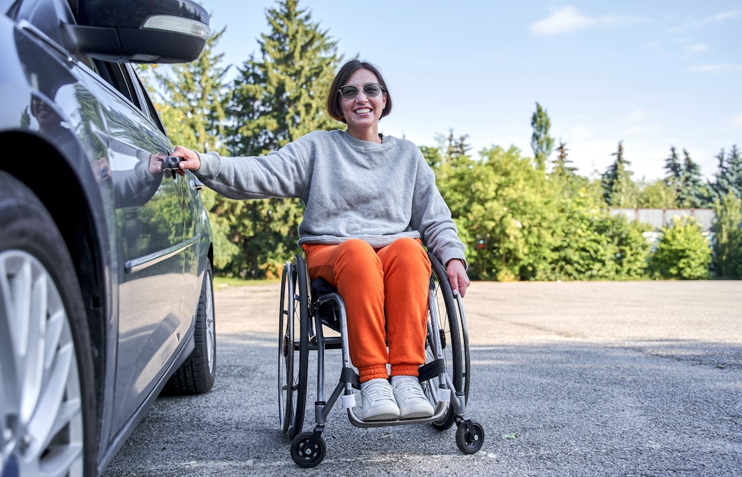 Frau im Rollstuhl mit grünen Tannenbäumen im Hintergrund