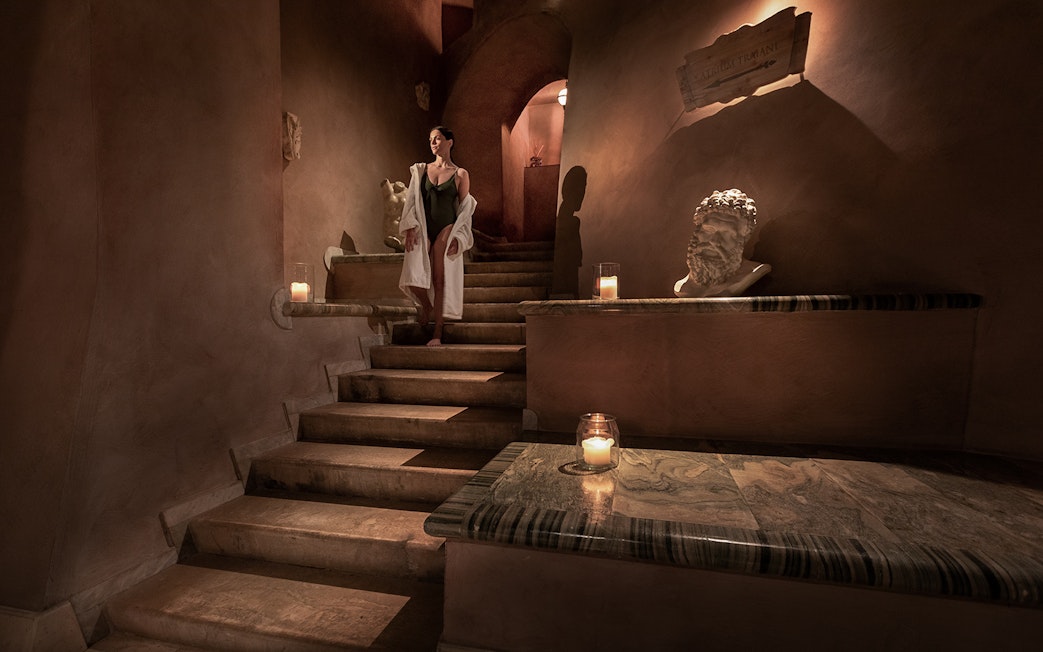 Woman in robe descending candlelit stone stairs at QC Terme Roma spa.