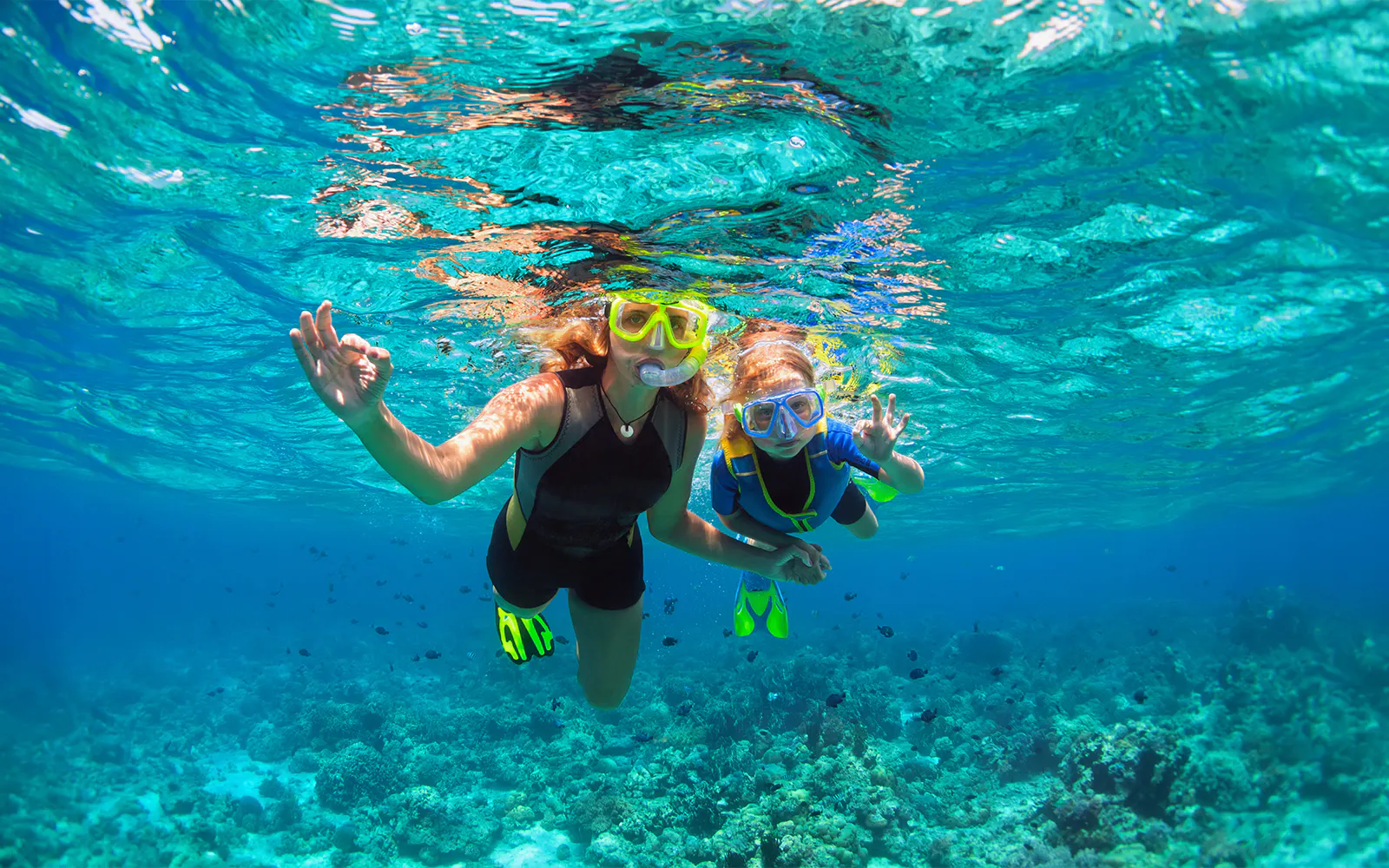 Mother and child snorkeling underwater with masks in clear blue ocean.