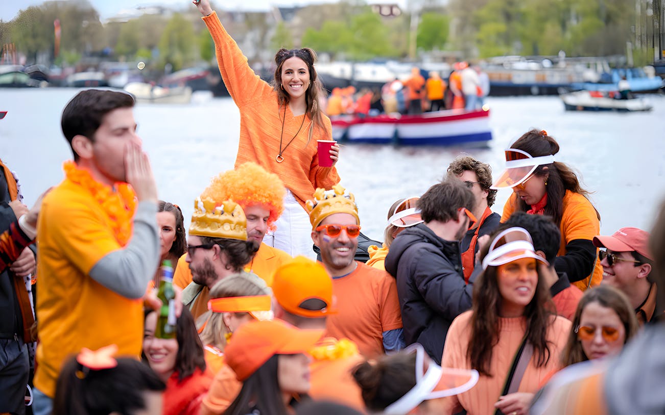 Crowd celebrating on a boat during Amsterdam King's Day party cruise, wearing orange outfits.