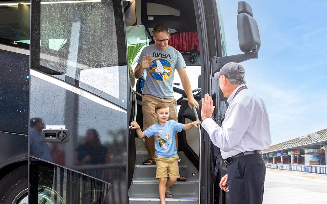 Visitors exiting a tour bus at Kennedy Space Center, greeted by a guide.