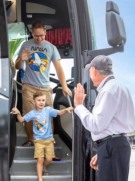 Visitors exiting a tour bus at Kennedy Space Center, greeted by a guide.