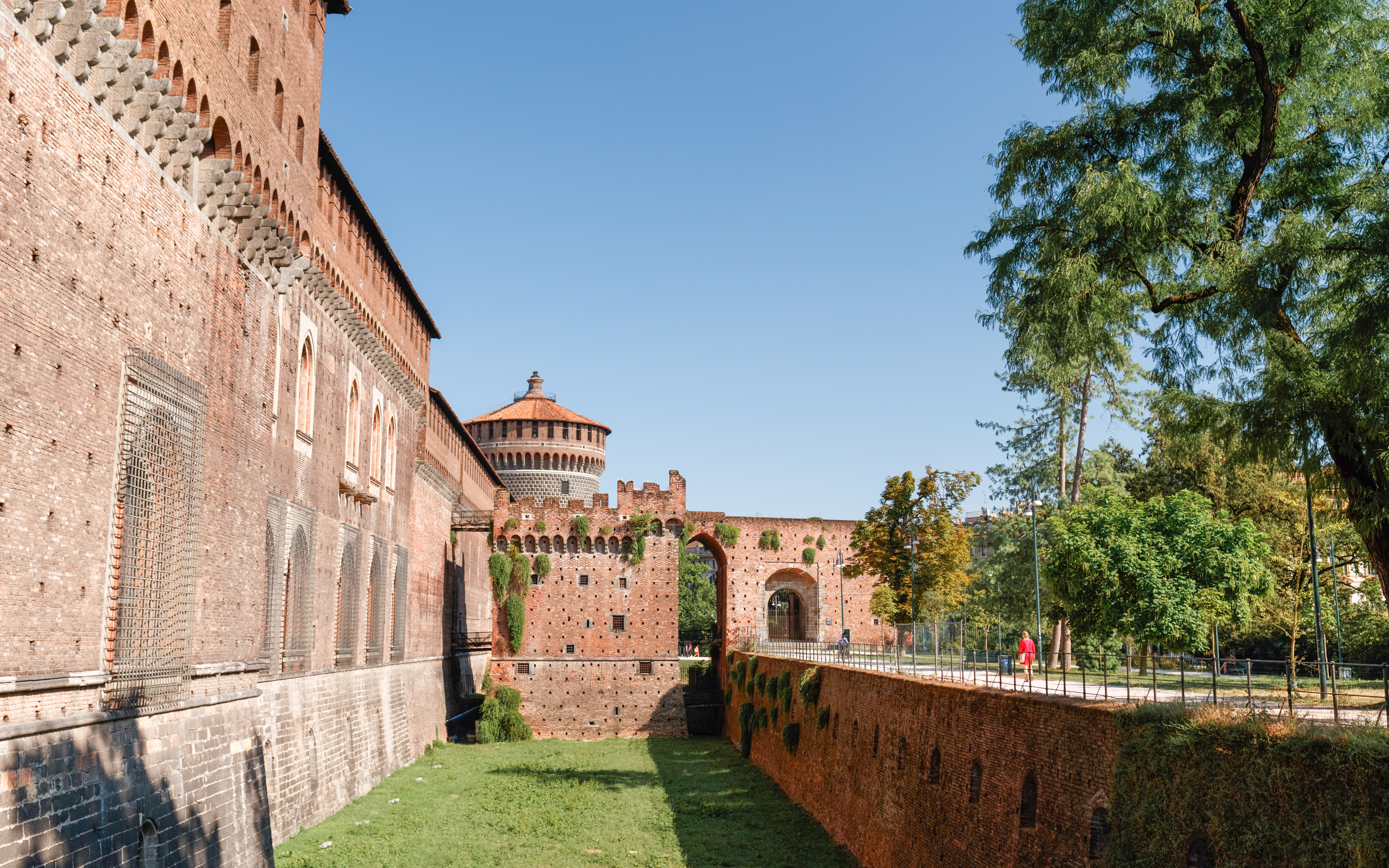 Sforza Castle Milan with brick walls and tower, surrounded by greenery.