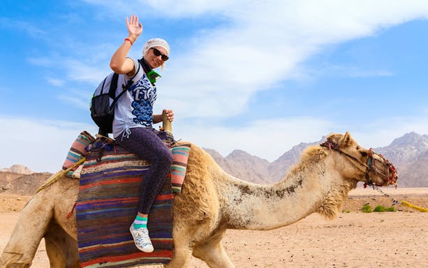 Traveler riding a camel in the Hurghada desert with mountains in the background.