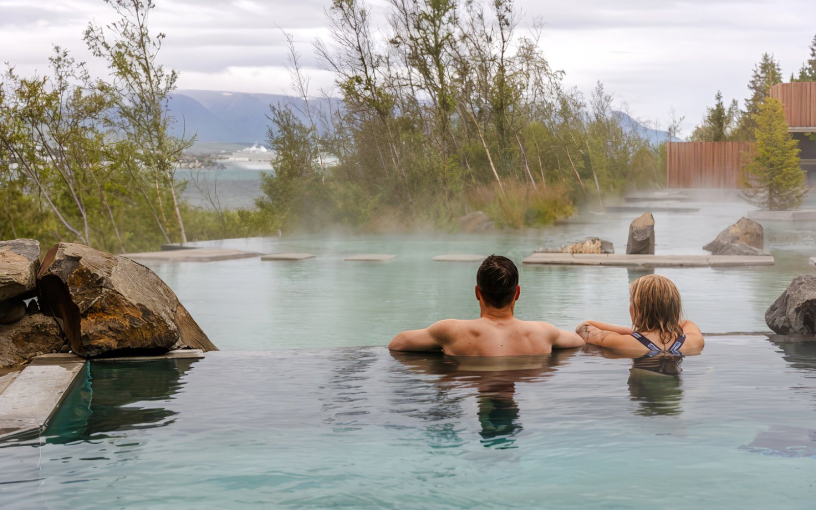 Couple relaxing in Forest Lagoon geothermal spa, surrounded by trees in Vaðlaskógur forest, near Akureyri, North Iceland.