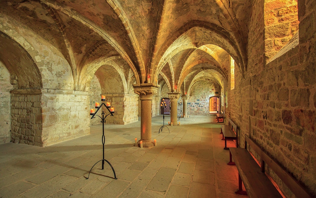 Mont-Saint-Michel Abbey interior with stone arches and candlelit stands.