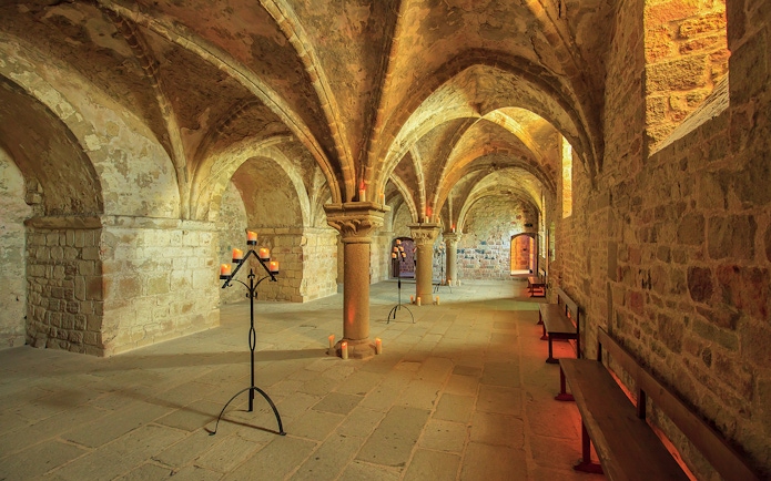Mont-Saint-Michel Abbey interior with stone arches and candlelit stands.