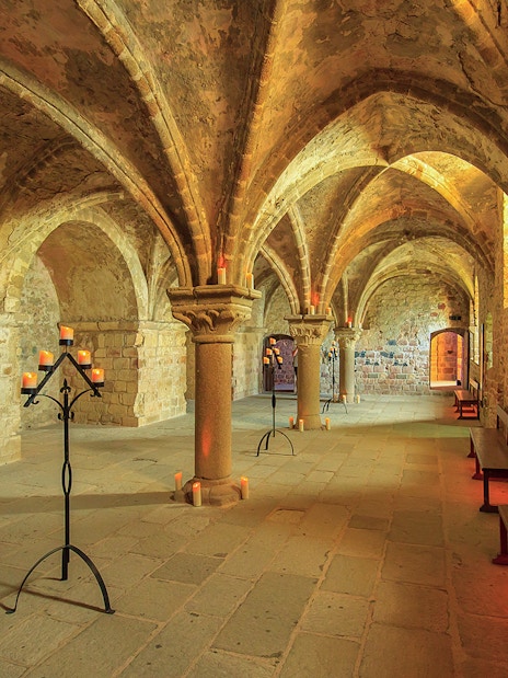 Mont-Saint-Michel Abbey interior with stone arches and candlelit stands.