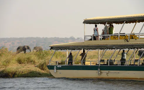 Boat safari on Chobe River with tourists viewing elephants on the riverbank in Botswana.
