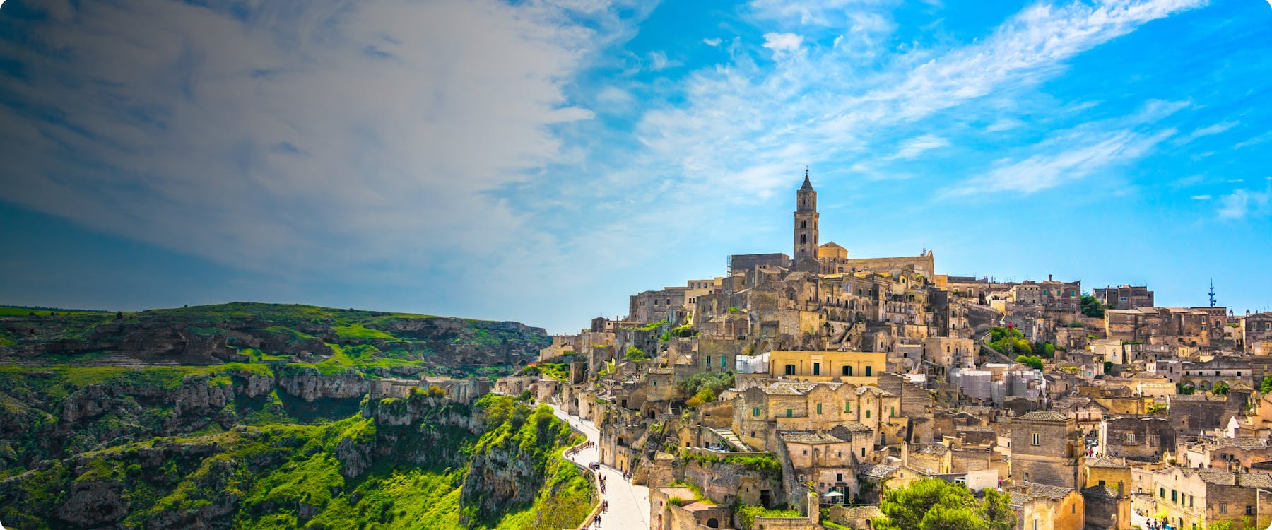 Matera's ancient stone cityscape with a prominent church tower under a blue sky.