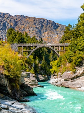 Bridge over Shotover River with turquoise water and rocky cliffs in Queenstown, New Zealand.