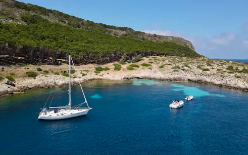 Sailboats anchored near the rocky coast of Favignana, Italy, with lush greenery in the background.