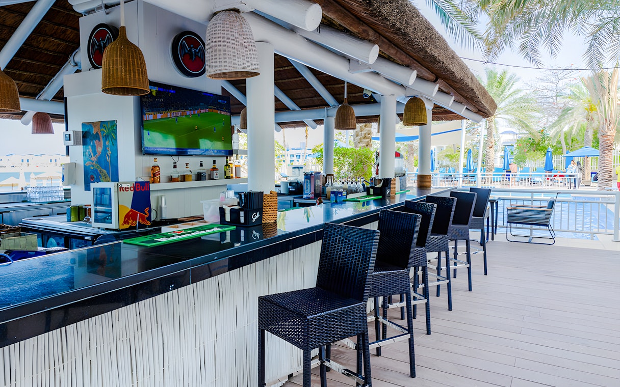 Outdoor bar area at Riva Beach Club with poolside seating and palm trees.