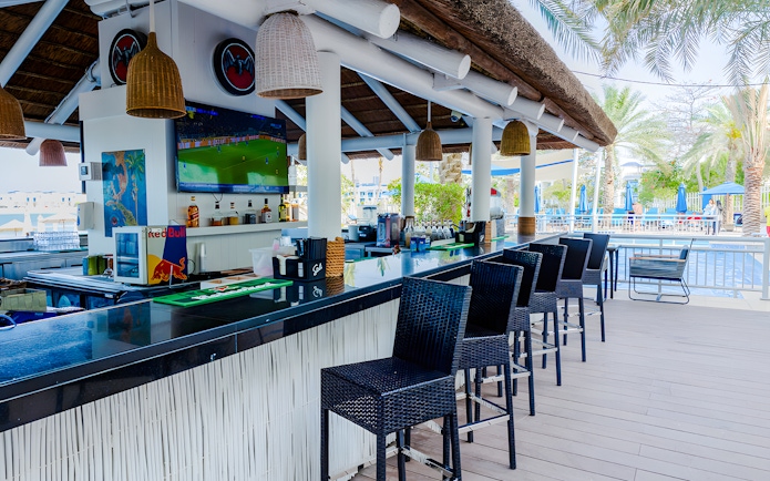 Outdoor bar area at Riva Beach Club with poolside seating and palm trees.