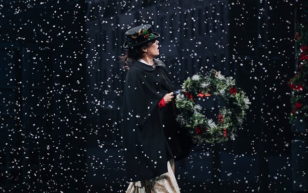 Person holding a Christmas wreath in falling snow, scene from A Christmas Carol.