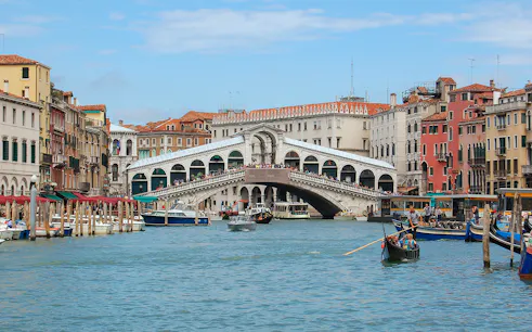 Rialto Bridge over the Grand Canal in Venice, Italy, with gondolas and historic buildings.