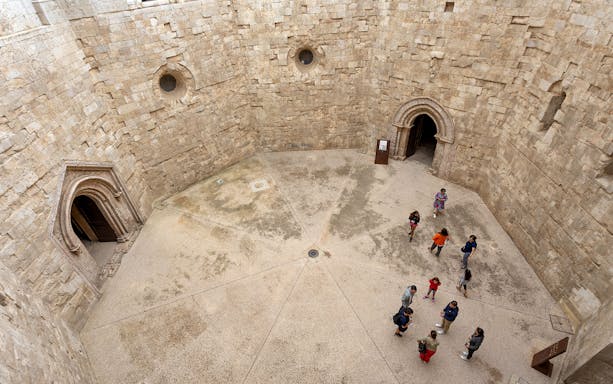 Tour group with guide inside Castel del Monte courtyard, Andria.
