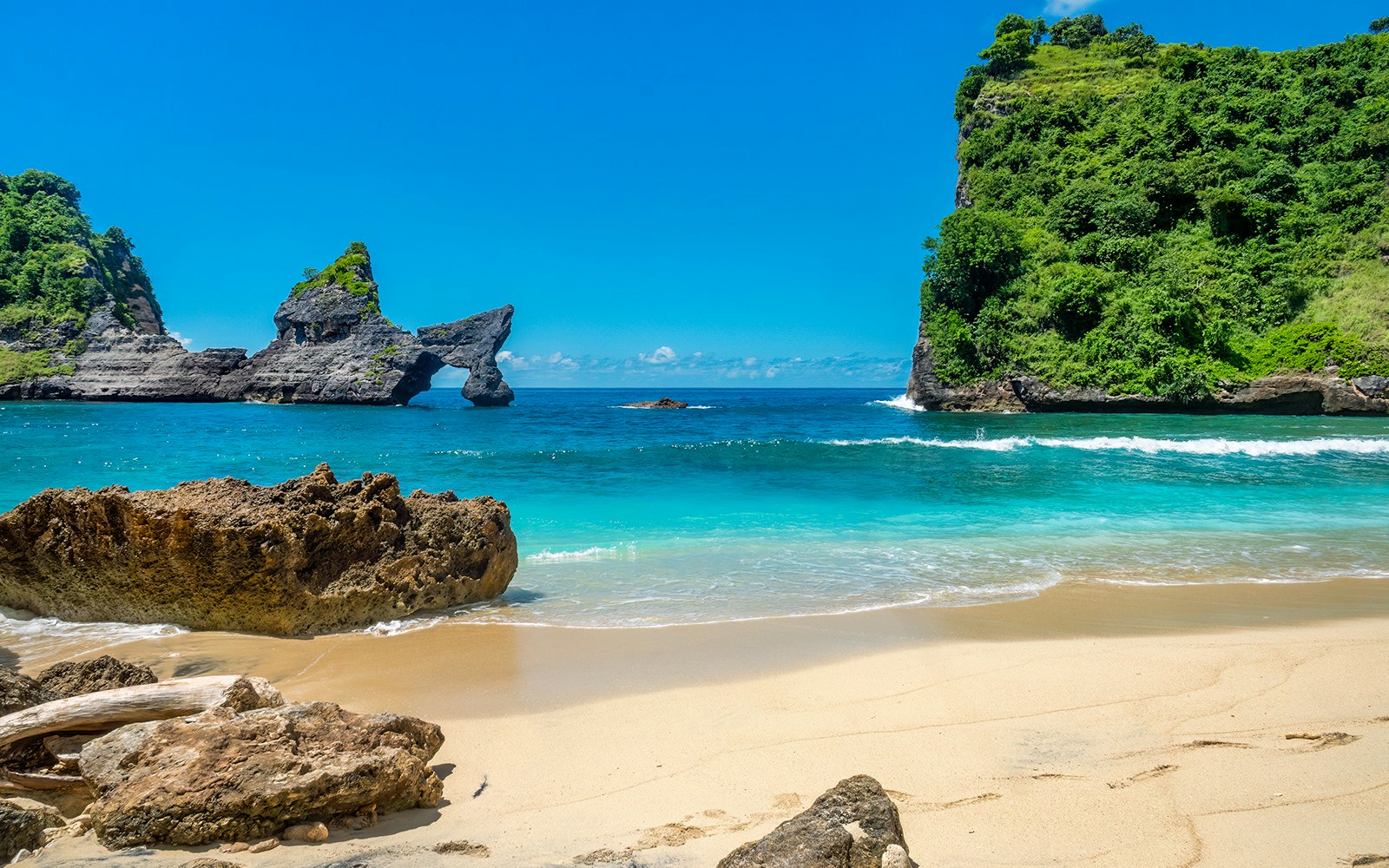 Tourists exploring the stunning Atuh Beach, Nusa Penida, with its unique cliff formations and clear blue waters
