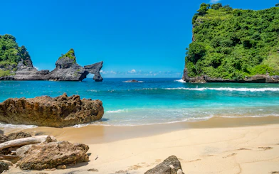 Tourists at Atuh Beach, Nusa Penida, with unique cliffs and clear blue waters.