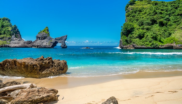 Tourists at Atuh Beach, Nusa Penida, with unique cliffs and clear blue waters.
