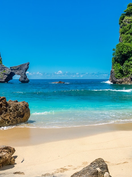 Tourists at Atuh Beach, Nusa Penida, with unique cliffs and clear blue waters.