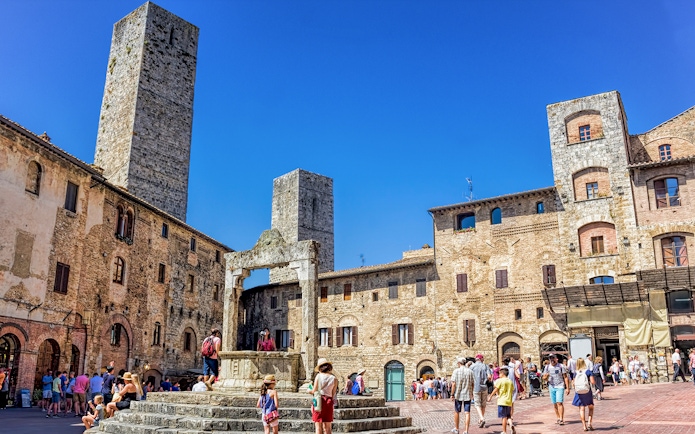 San Gimignano square with medieval towers and tourists exploring the historic architecture.