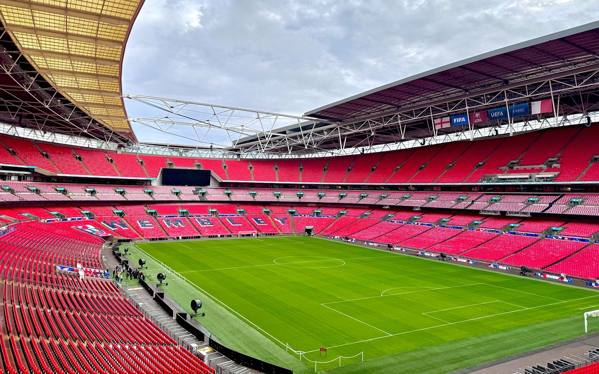 Wembley Stadium interior with empty red seats and green pitch, London.
