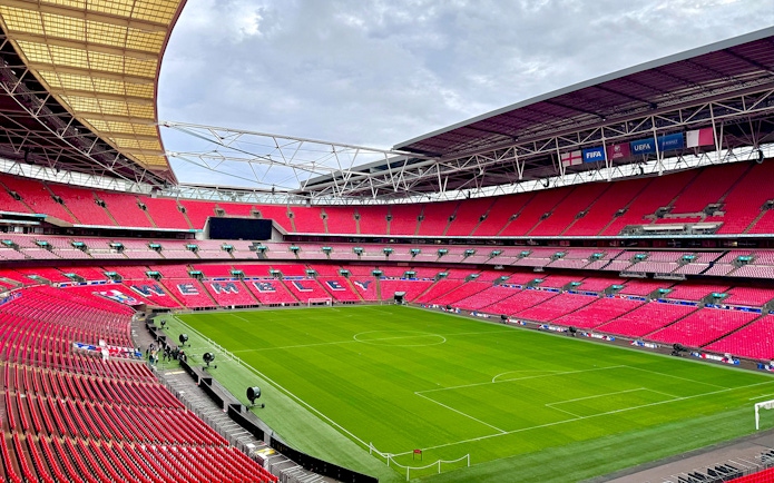 Wembley Stadium interior with empty red seats and green pitch, London.
