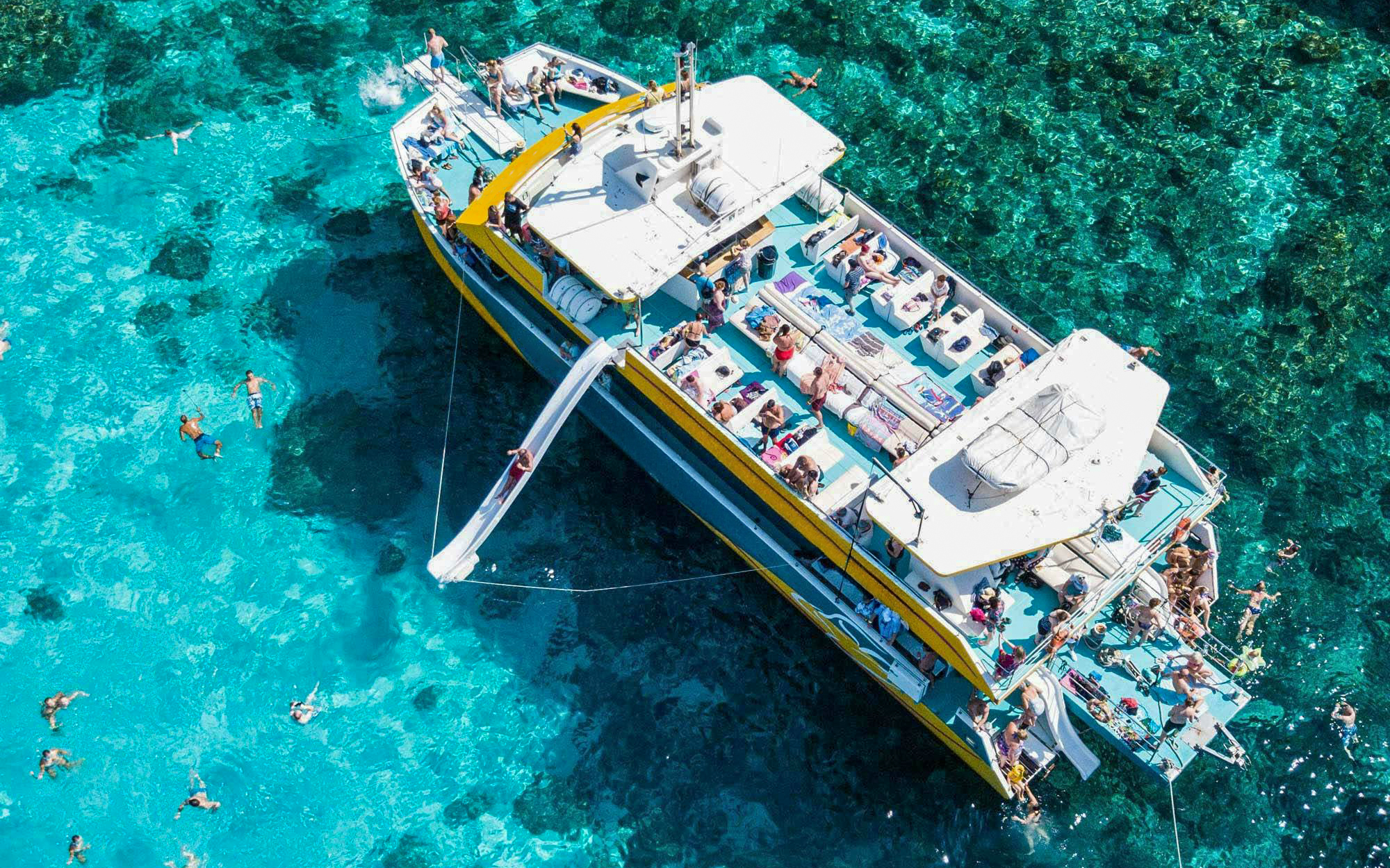 Aerial view of a boat with a slide at Blue Lagoon, people swimming nearby.