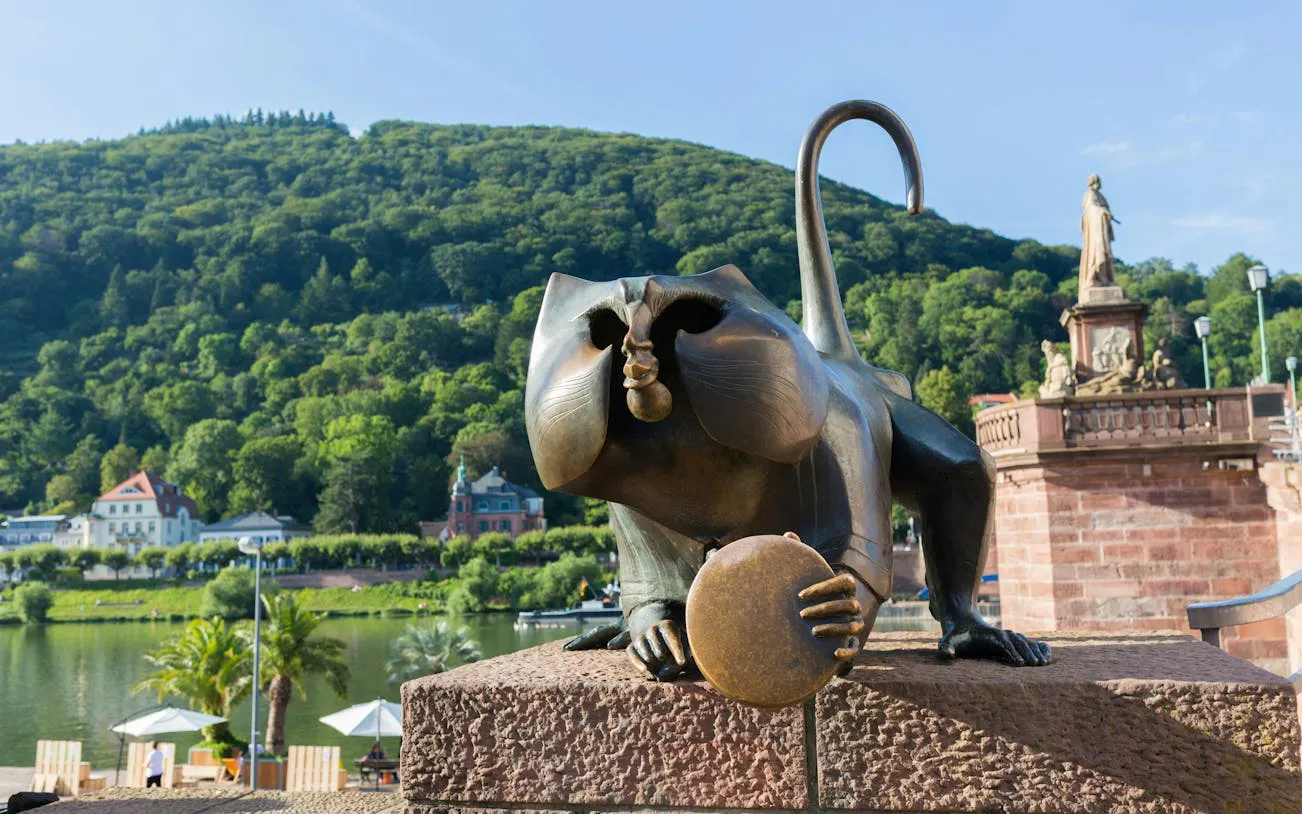 Heidelberg Bridge Monkey statue with scenic hillside backdrop.