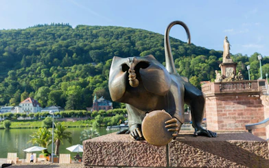 Heidelberg Bridge Monkey statue with scenic hillside backdrop.