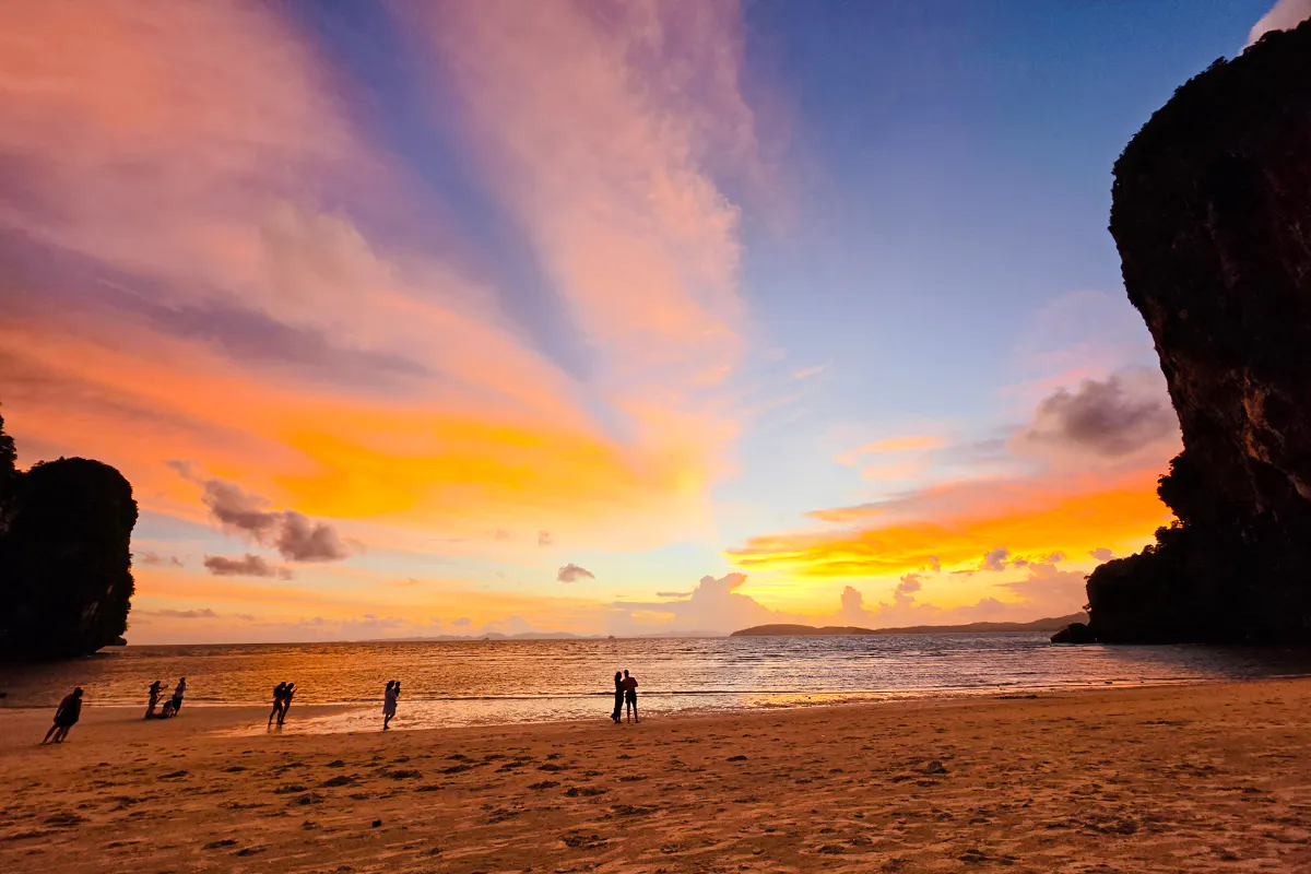 Sunset at Railay Beach, Krabi with silhouettes of people on the shore and vibrant sky colors.