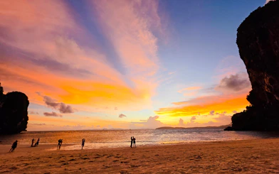 Sunset at Railay Beach, Krabi with silhouettes of people on the shore and vibrant sky colors.