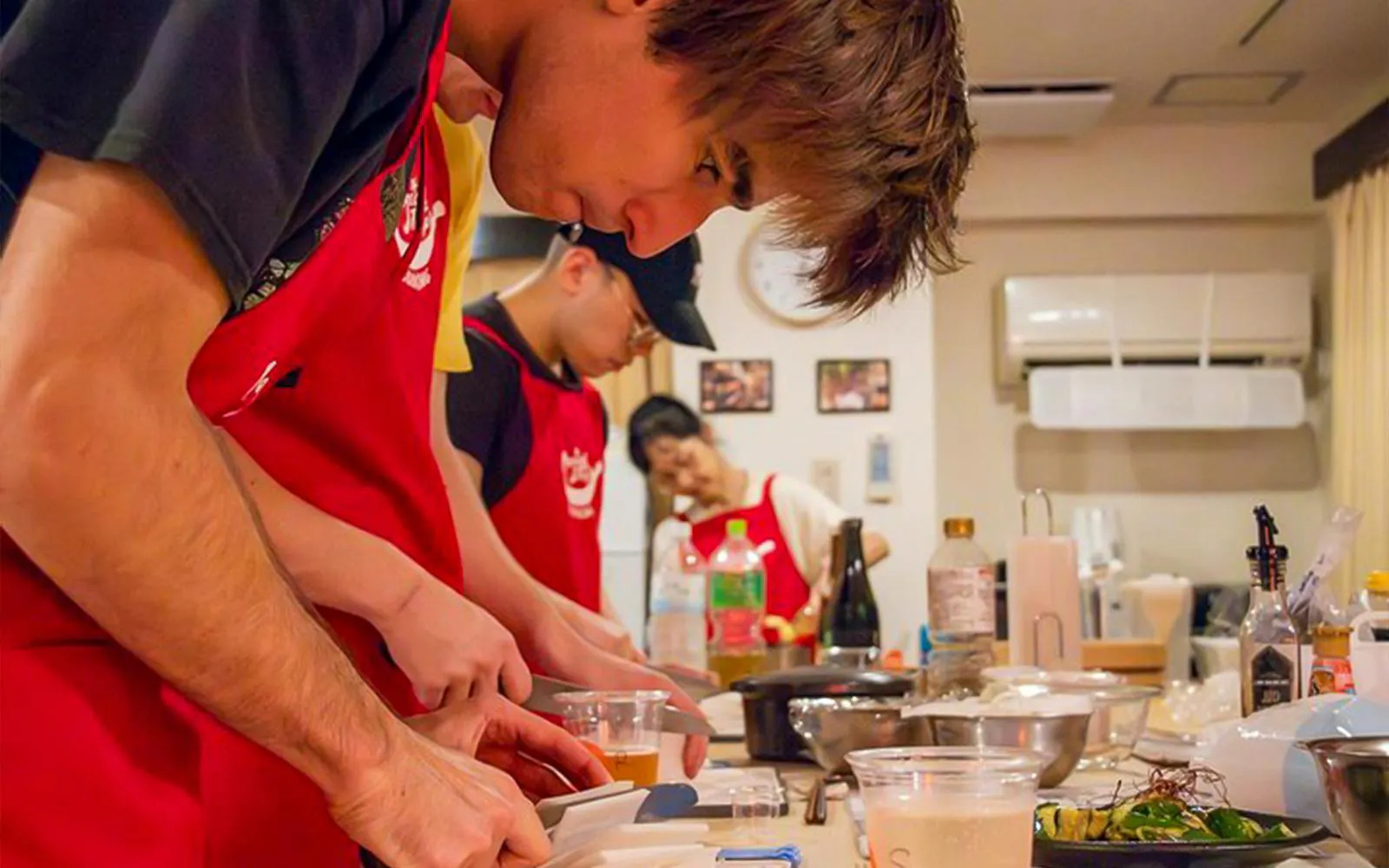 Participants preparing food in a Tokyo izakaya-style cooking class with drinks and ingredient shopping.