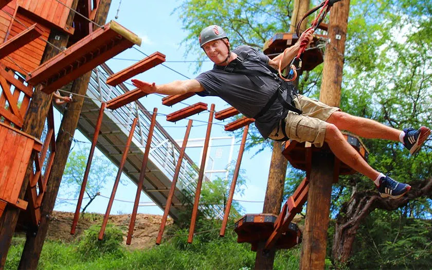 Participant on high-elevation adventure course with safety gear, navigating wooden elements.