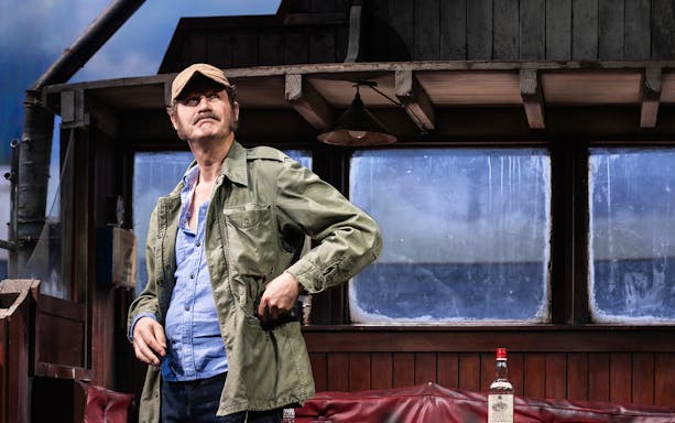Man in a cap and jacket on a boat set from "The Shark is Broken" play.