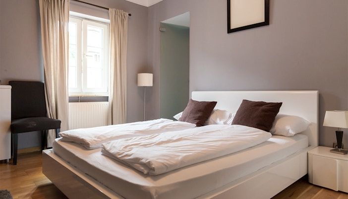 Modern hotel room with double bed, white linens, and brown pillows near a window.