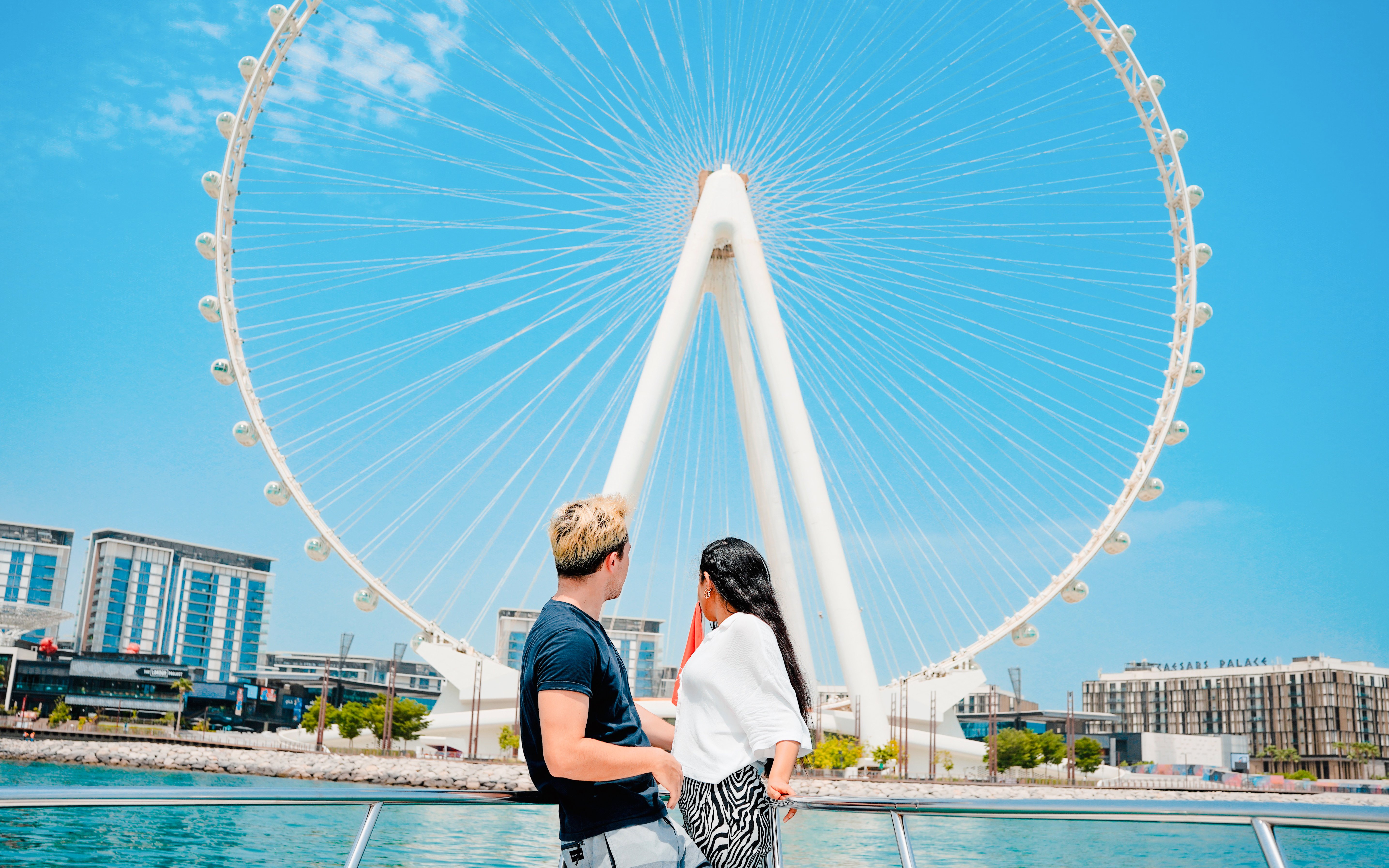 Couple on yacht with view of Ain Dubai Ferris wheel at Dubai Harbour.