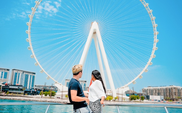 Couple on yacht with view of Ain Dubai Ferris wheel at Dubai Harbour.
